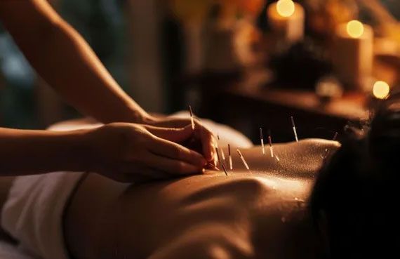 Unas manos masajean la espalda de una persona con aceite en un ambiente de spa con luz tenue y cálida.