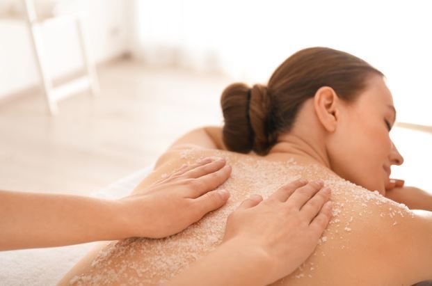 Mujer recibiendo un tratamiento de exfoliación corporal en un spa.