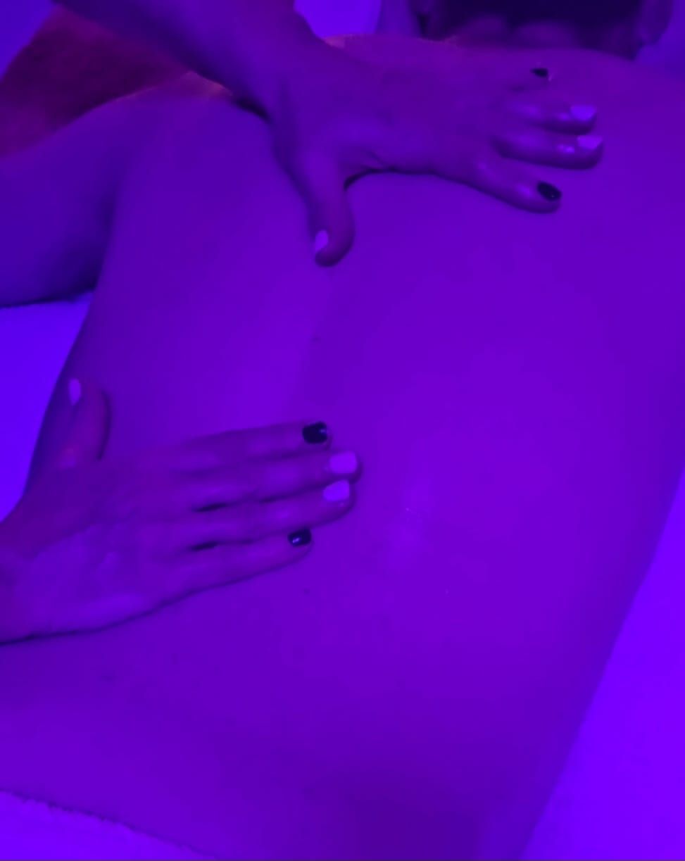 Manos masajeando una espalda bajo luz violeta.
