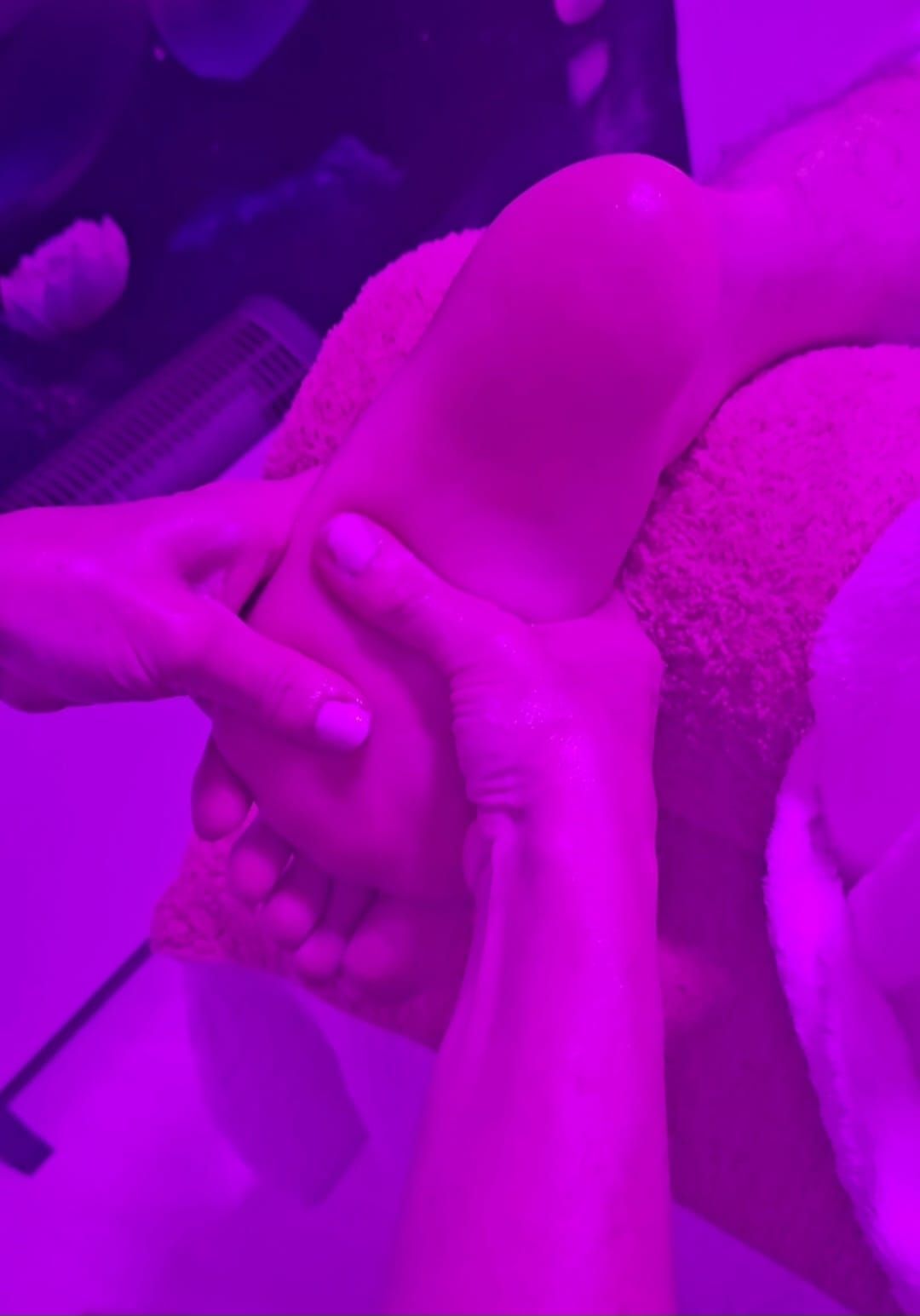 Unas manos masajeando un pie bajo una iluminación violeta.