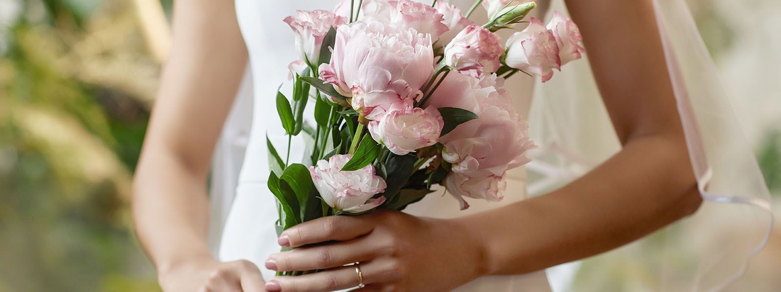 Eine Braut im Hochzeitskleid hält einen Strauß rosa Blumen in der Hand.