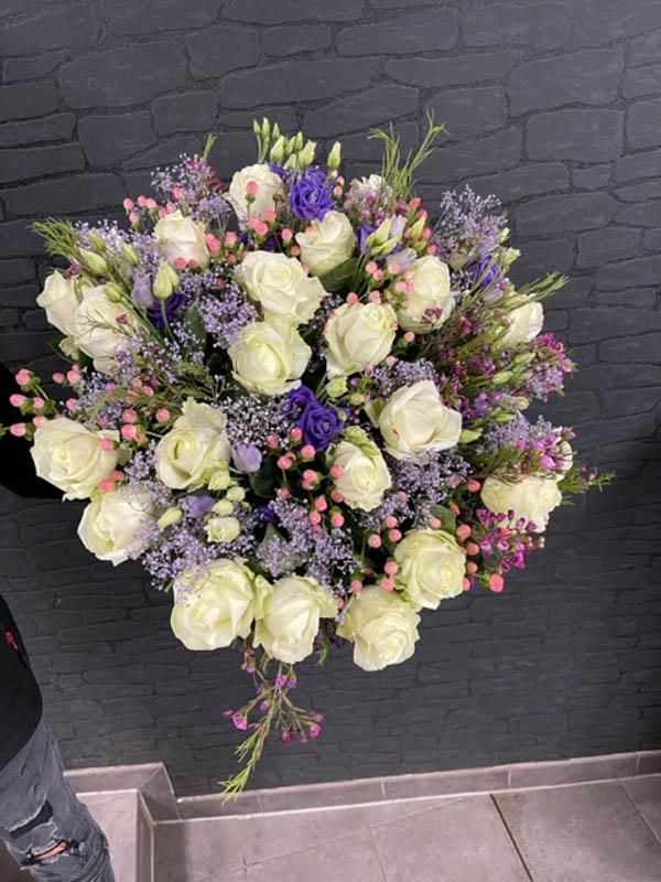 Eine Person hält einen großen Strauß weißer Rosen und violetter Blumen.