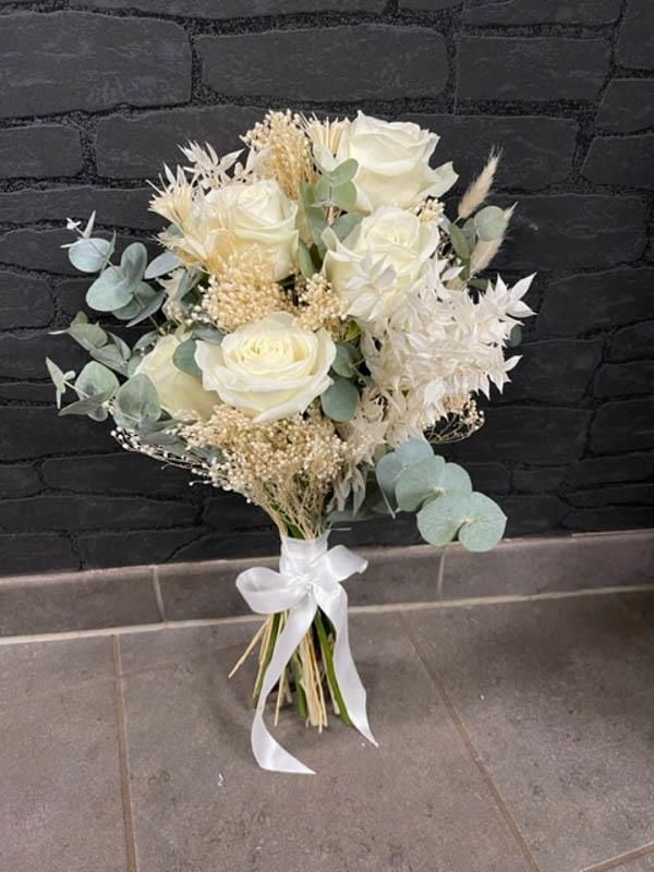 Ein Strauß weißer Blumen mit einer weißen Schleife steht auf einem gefliesten Boden.