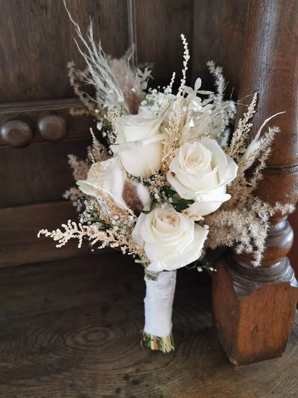 Ein Strauß weißer Rosen steht auf einem Holztisch.