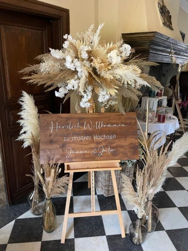 Ein Holzschild steht auf einer Holzstaffelei, umgeben von Blumen.