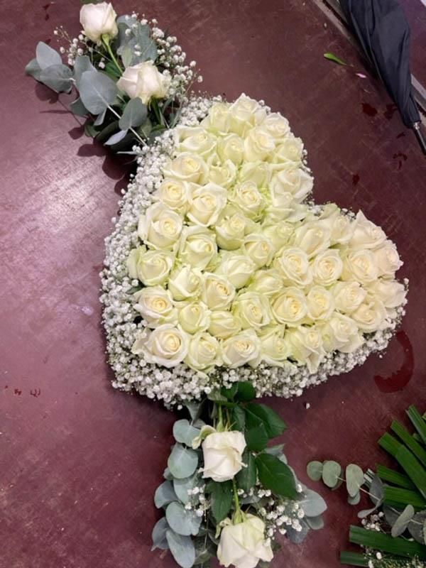 Auf einem Tisch steht ein Herz aus weißen Rosen und Schleierkraut.