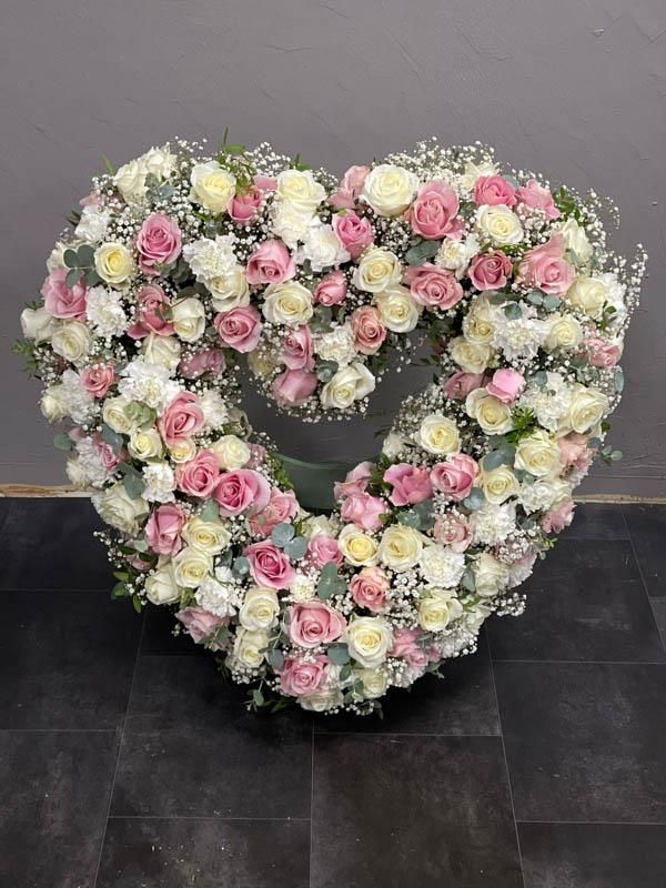 Ein herzförmiger Kranz aus rosa und weißen Rosen und Schleierkraut.