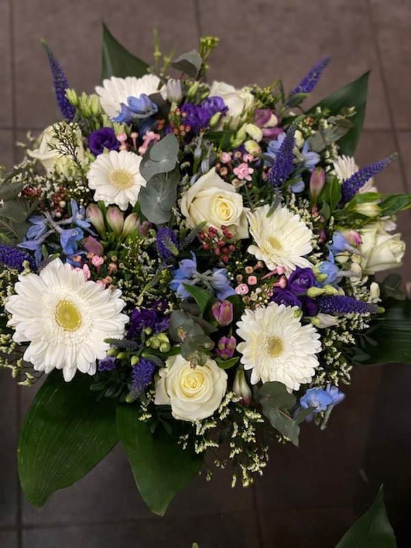 Auf einem Tisch steht ein Strauß weißer und violetter Blumen.