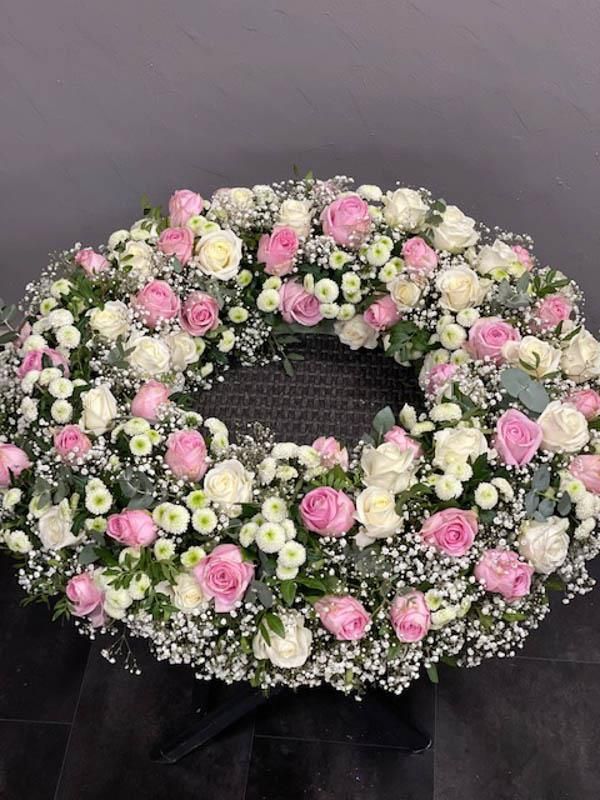Auf einem Tisch steht ein Kranz aus rosa und weißen Blumen.