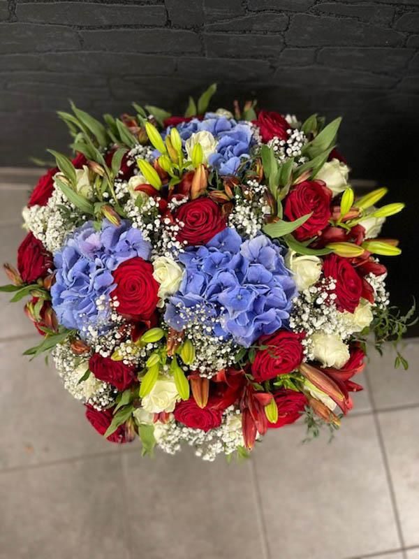 Auf einem Tisch steht ein Strauß roter, weißer und blauer Blumen.