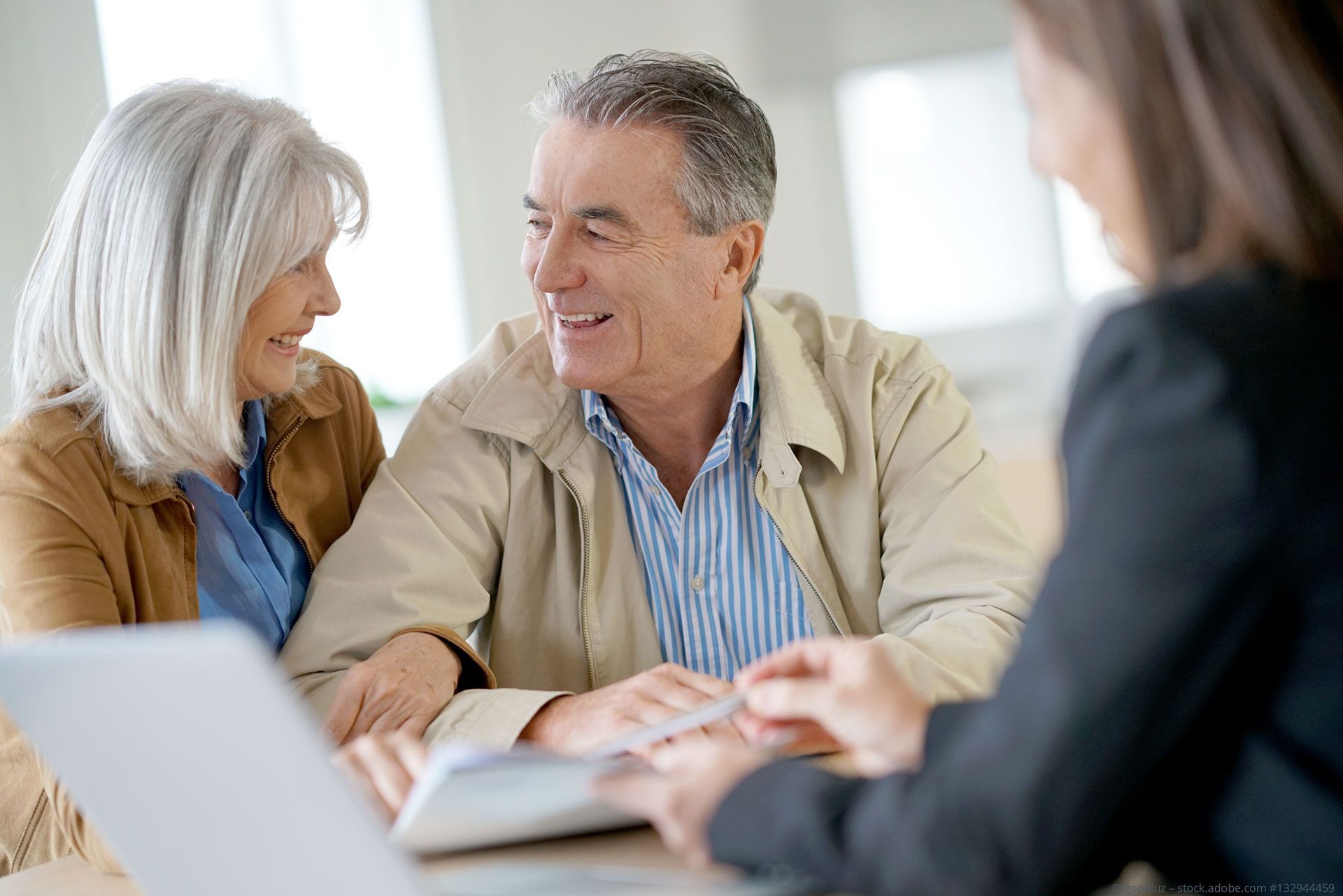 Senior couple smiles while meeting with financial advisor.