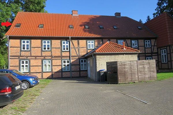 Half-timbered building with a red tiled roof, windows, and a small extension, cars parked in front.
