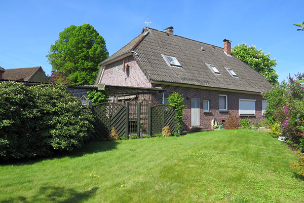 A two-story brick house with a sloping roof and a green lawn on a sunny day.