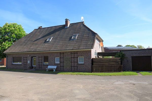 House with brick facade, green lawn, fence, and blue sky.