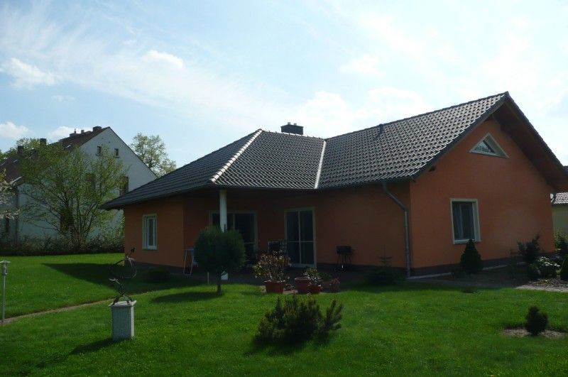 Neubau eines Einfamilienhauses mit orangebrauner Fassade und dunklem Dach. Im Vordergrund ein Garten mit großer Gartenfläche.