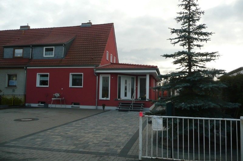 Modernisierung eines Einfamilienhauses mit roter Fassade, rotem Dach und mit Steinen gepflasterter Auffahrt.