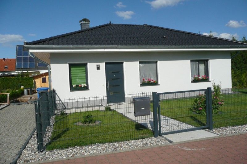 Neubau eines Einfamilienhauses mit weißer Fassade und dunklem Dach, dass farblich passend zu den Fenstern und der Eingangstür passt.