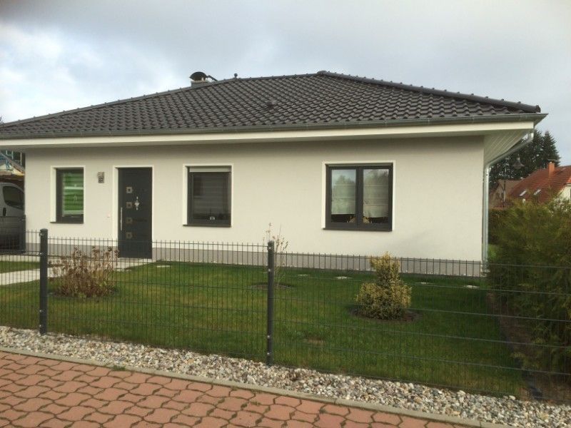 Neubau Einfamilienhaus mit heller Fassade und Dach, Fenstern und Tür, die farblich abgestimmt sind in einem dunklen grau-grün.