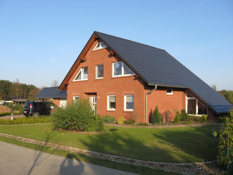 Neubau Einfamilienhaus mit orangefarbener Fassade und dunklem Dach, davor ein Garten mit viel Rasenfläche.