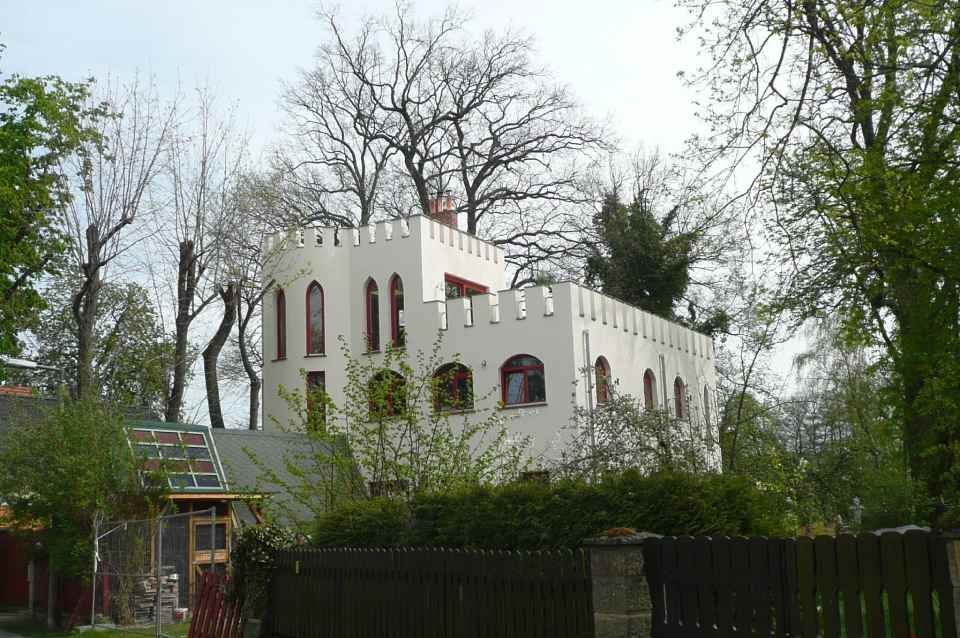 Schlösschen mit Erker und Zinnen mit weißer Fassade und roten Fenstern.