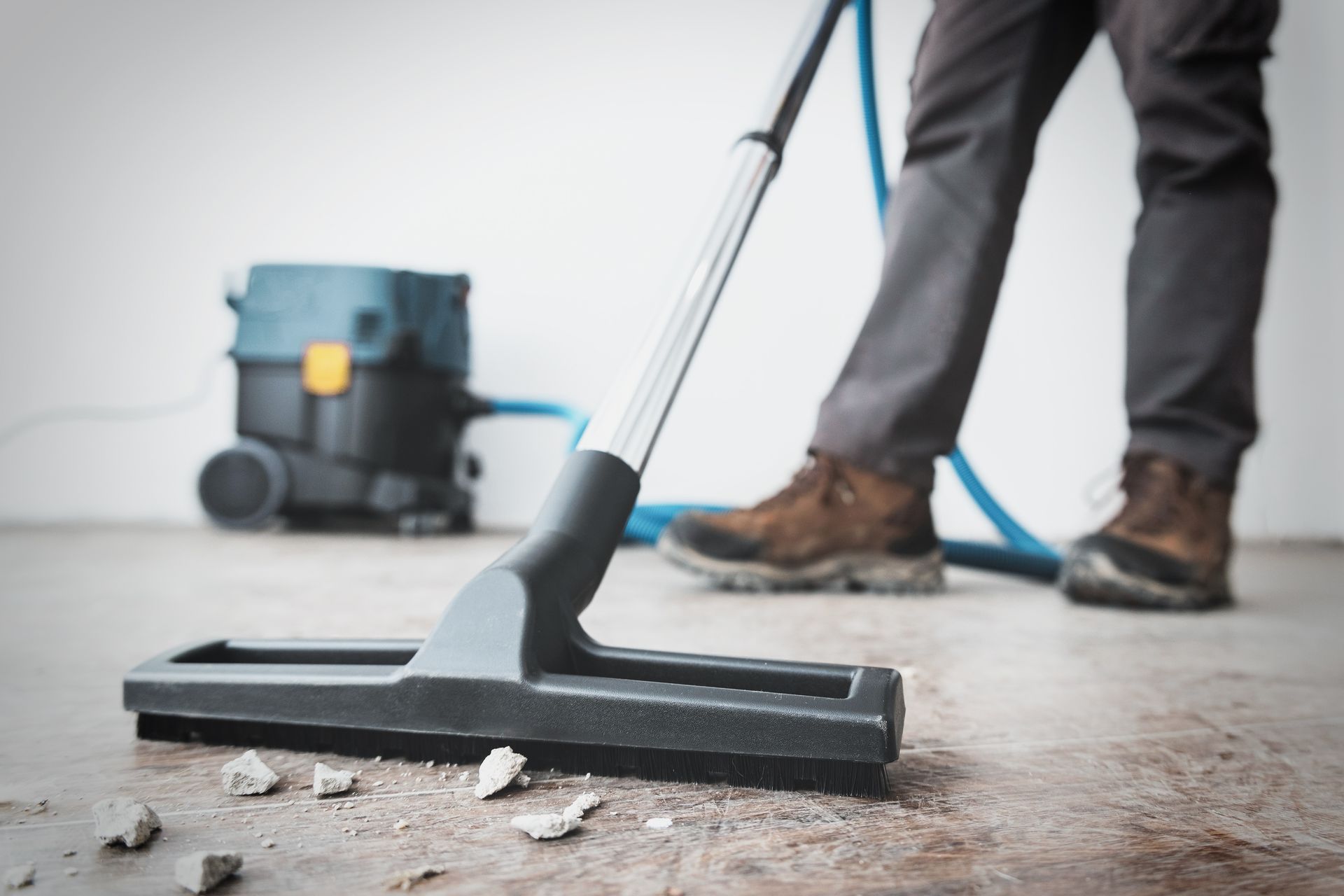 Eine Person benutzt einen Industriesauger, um Bauschutt von einem Betonboden zu entfernen.