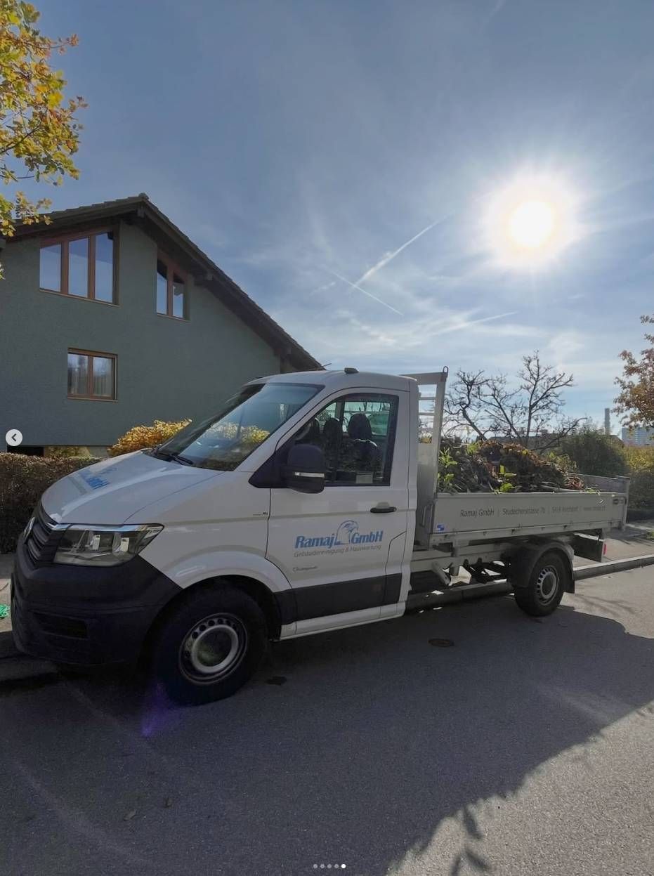 Ein weisser Pickup-Truck mit Gartenabfällen auf der Ladefläche parkte unter strahlend blauem Himmel vor einem grauen Haus.