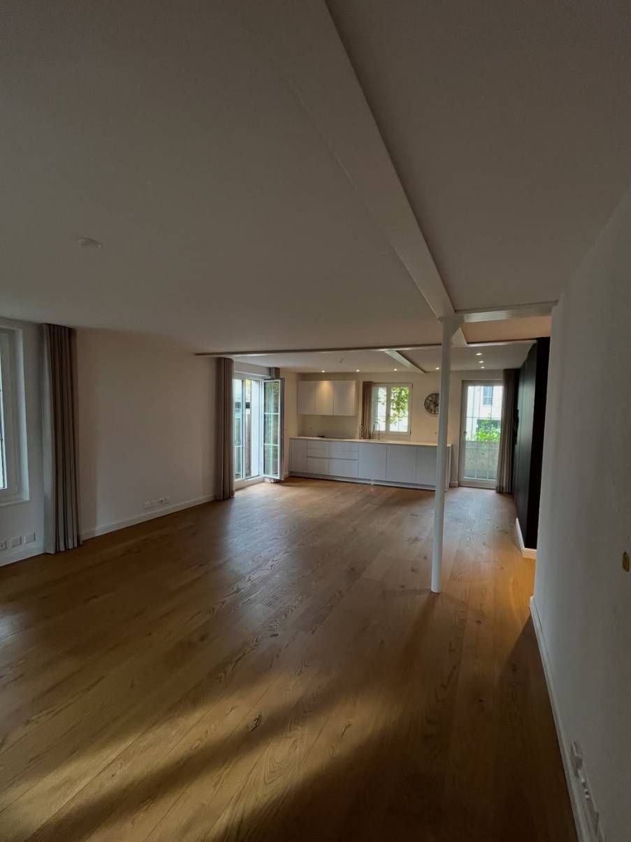 Eine helle, offene Wohnung mit hellen Holzböden, einer zentralen Stützsäule und einer im hinteren Bereich sichtbaren Küche.