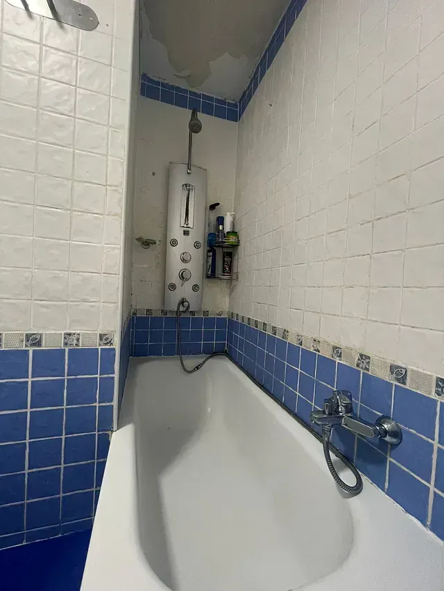 Una bañera en un baño con azulejos azules y ducha.