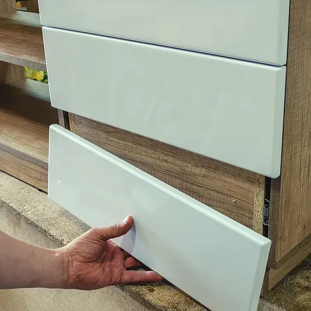 Una persona está abriendo un cajón blanco en un armario de madera.