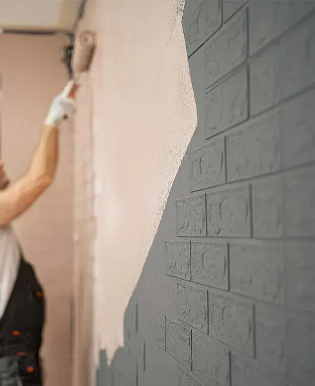 Una mujer está pintando una pared de ladrillos con un rodillo de pintura.