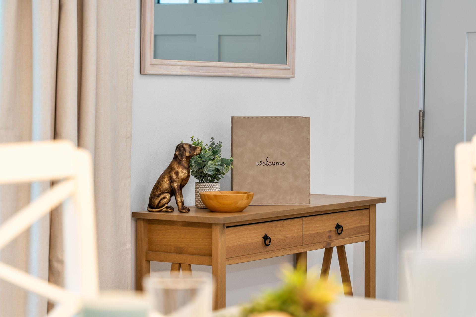 Wooden console table with a cat figurine, plant, and bowl in a bright room.