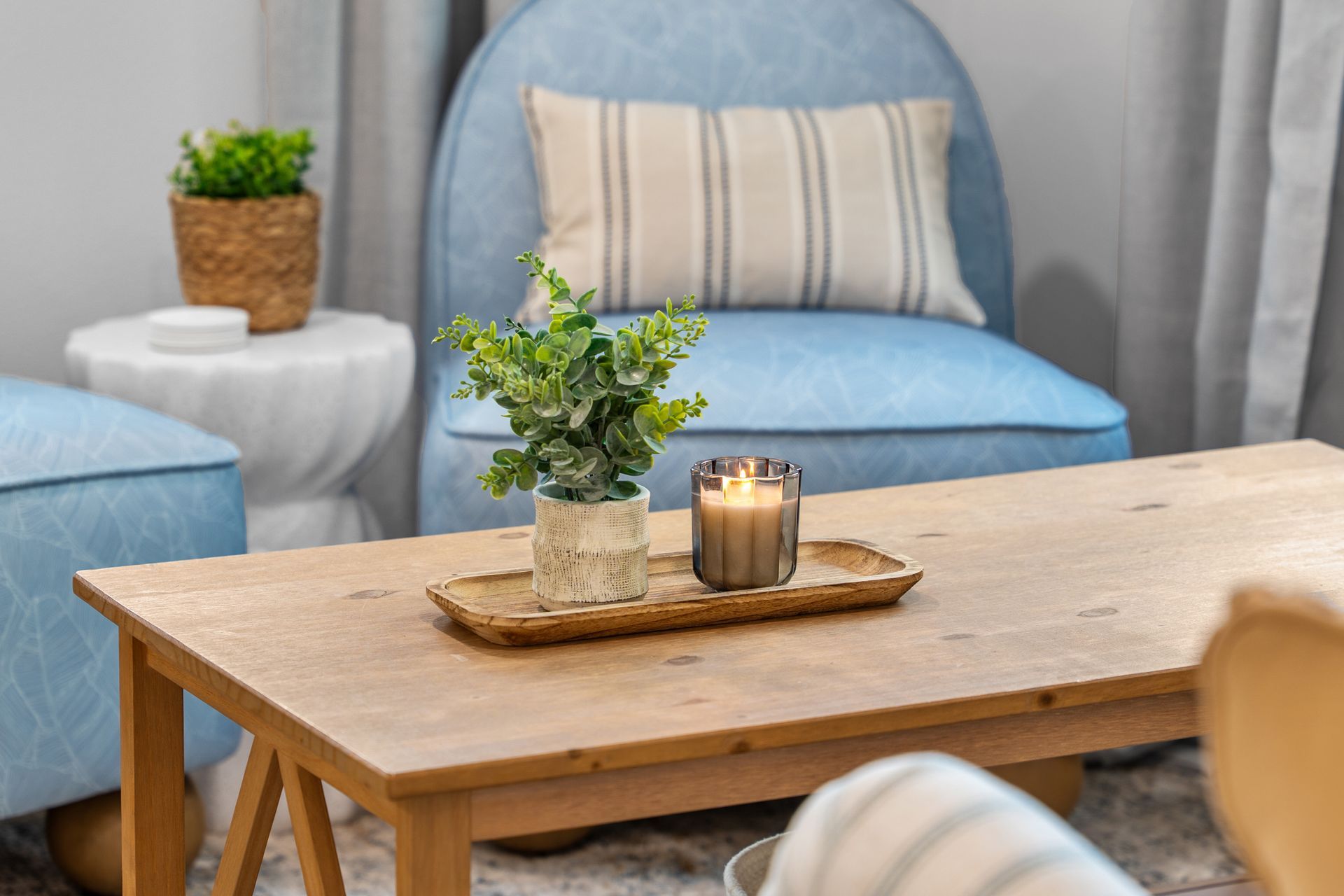 Cozy living room with blue chair, wooden coffee table, plants, and a lit candle