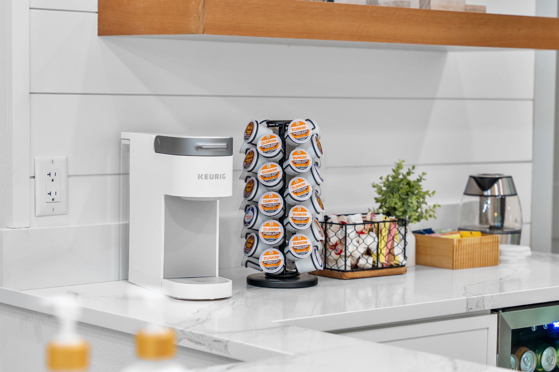 Coffee maker and pods on a white kitchen counter with small decor and a plant