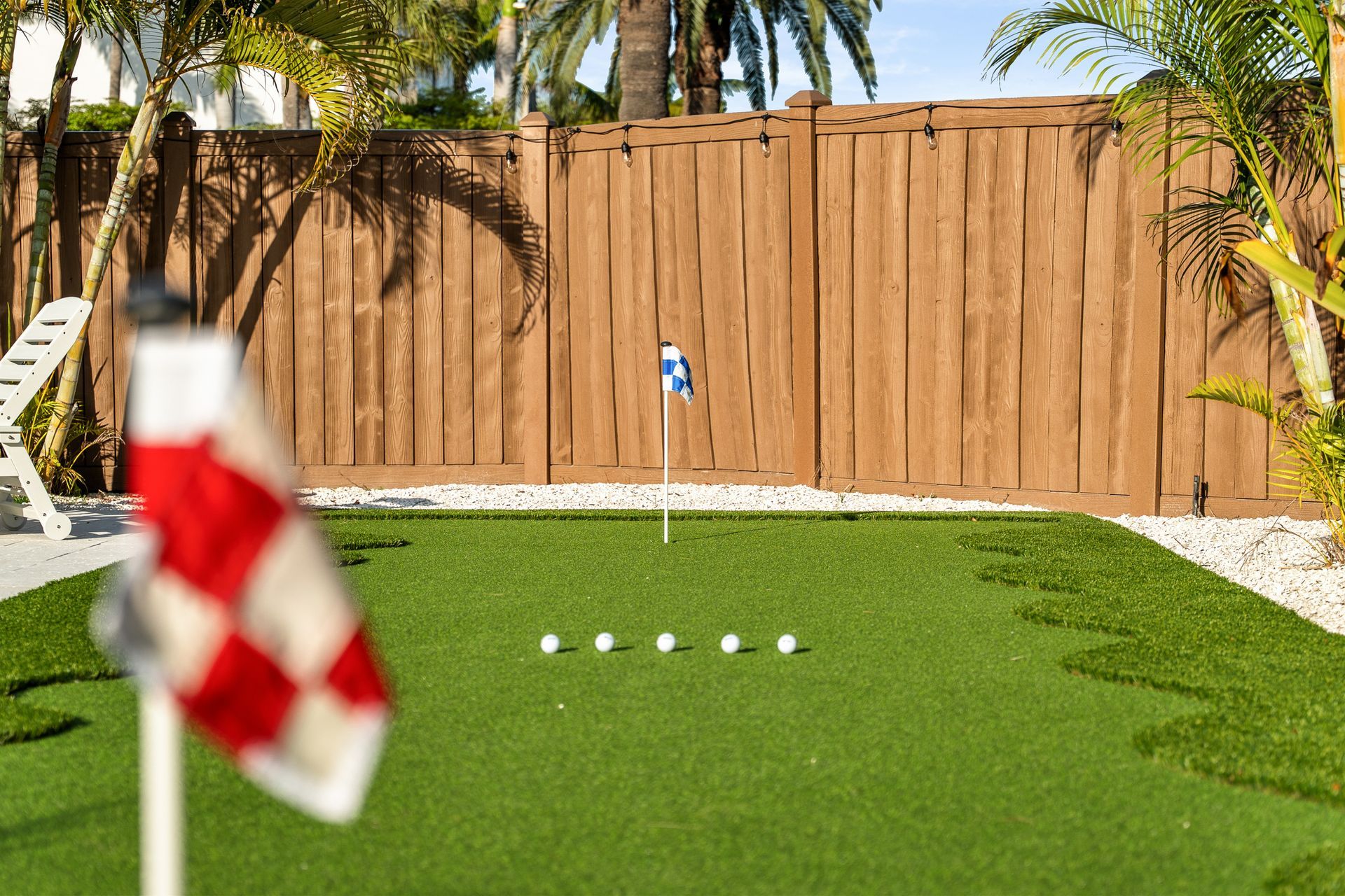 Mini golf green with four balls lined up near a hole, palm trees and wooden fence in the background.