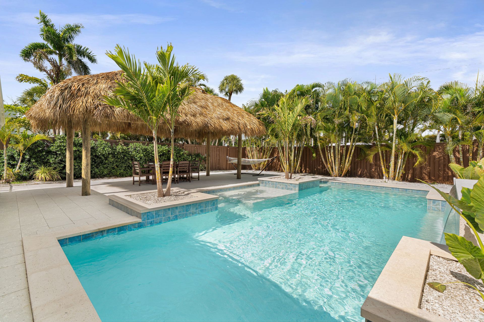Tropical resort pool with thatched cabana, lounge chairs, and palm trees under a bright sky