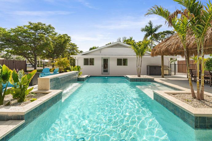 Luxury backyard with turquoise pool, white house, palm trees, and lounge area under bright sun