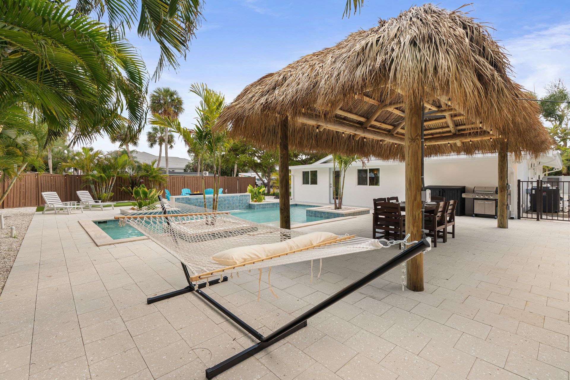 Poolside patio with thatched cabana, lounge chairs, and palm trees in a bright tropical resort setting