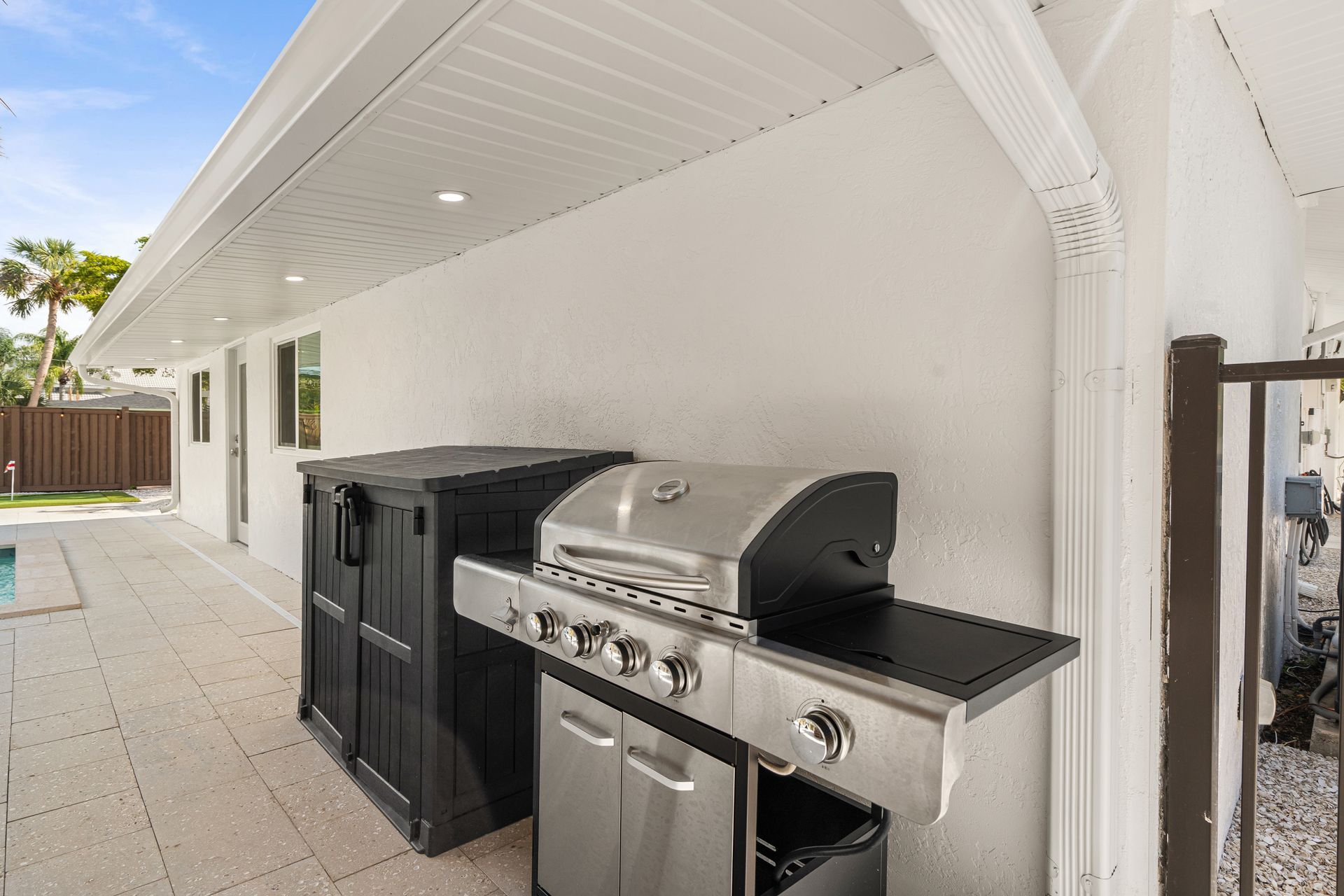 Outdoor patio with a stainless steel grill and black storage cabinets against a white wall