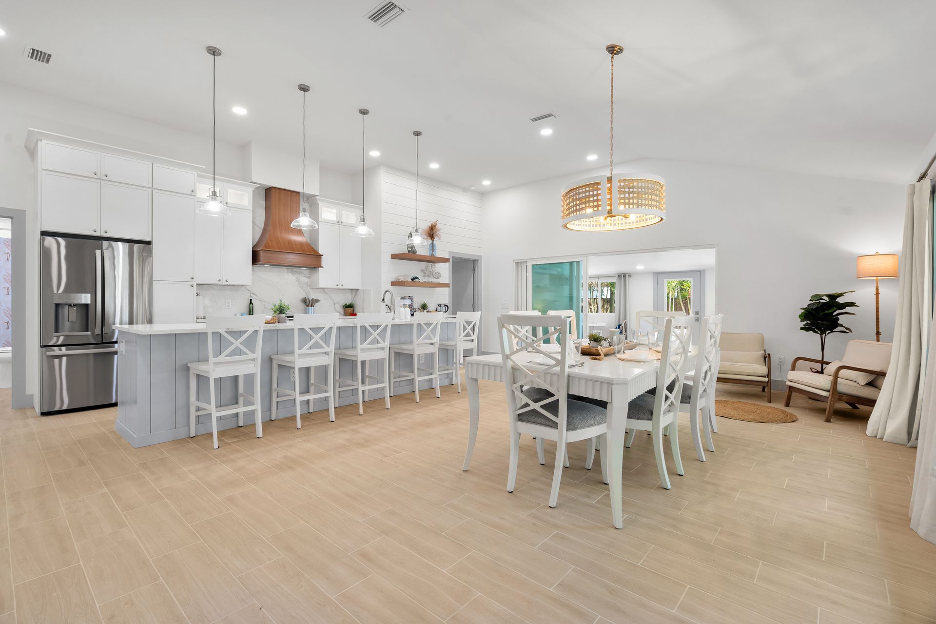 Bright open-plan kitchen and dining room with white furniture, light wood floors, and modern pendant lights