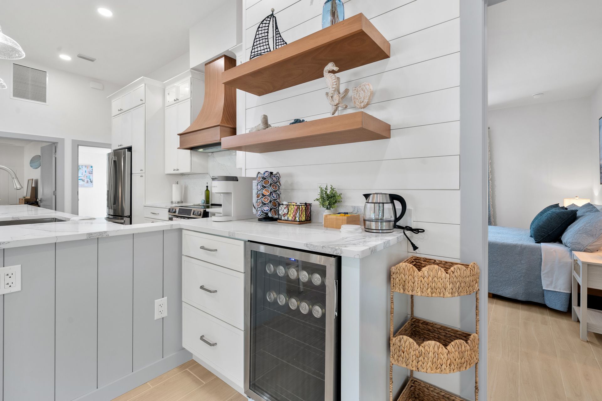 Bright white kitchen with open wood shelves, gray cabinets, and a small bar cart beside a doorway.