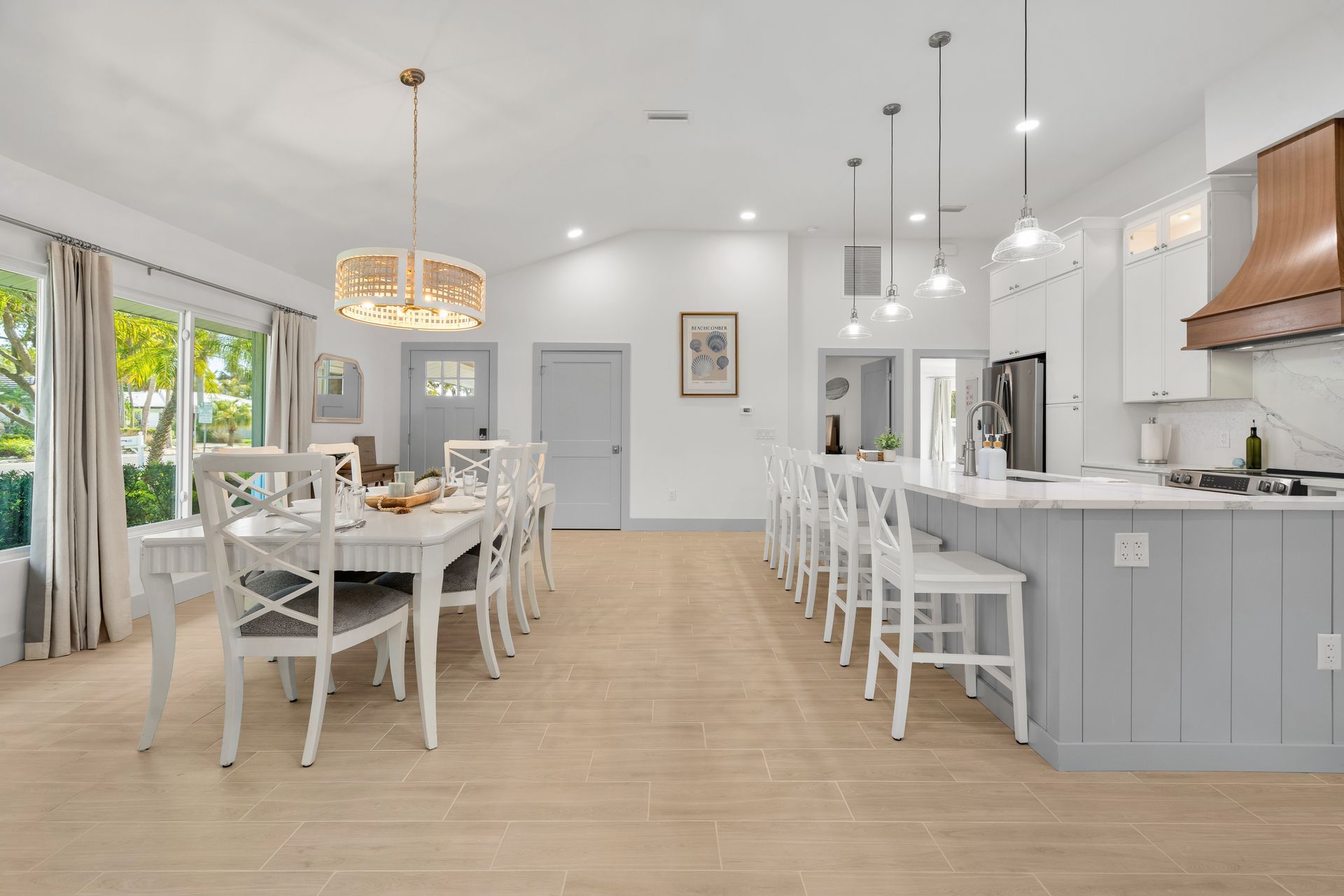 Bright open kitchen and dining area with white chairs, gray cabinets, and light wood floors