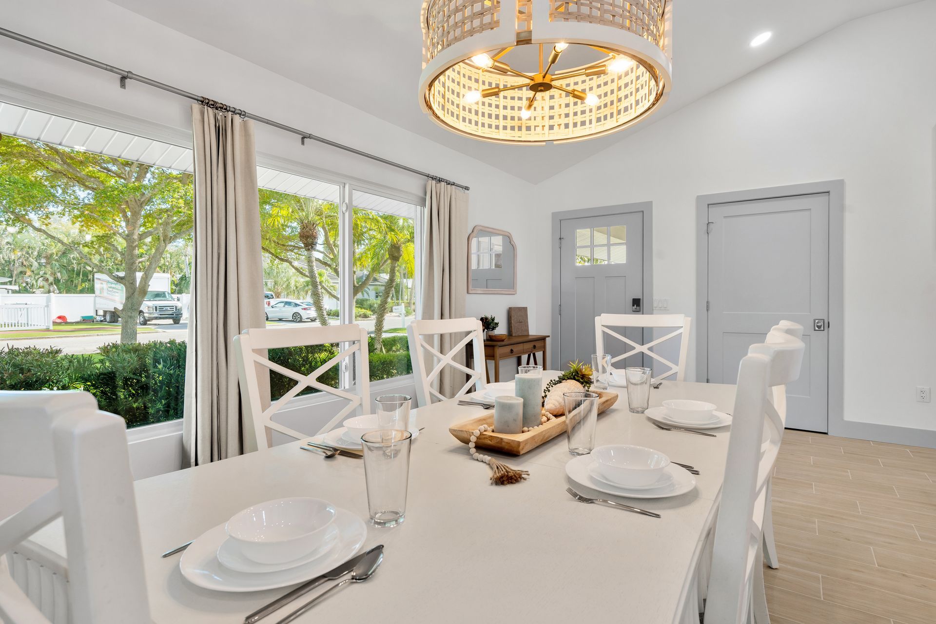 Bright dining room with white table setting, chandelier, and large windows overlooking greenery