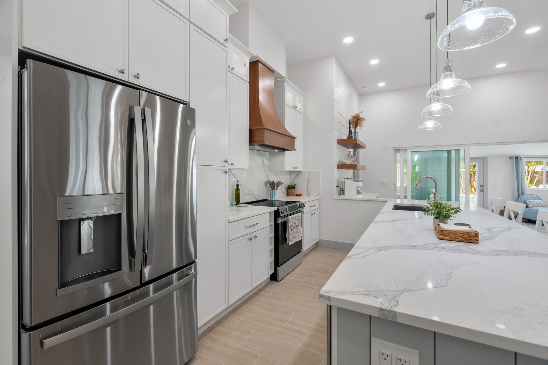 Modern white kitchen with stainless steel fridge, marble island, and pendant lights