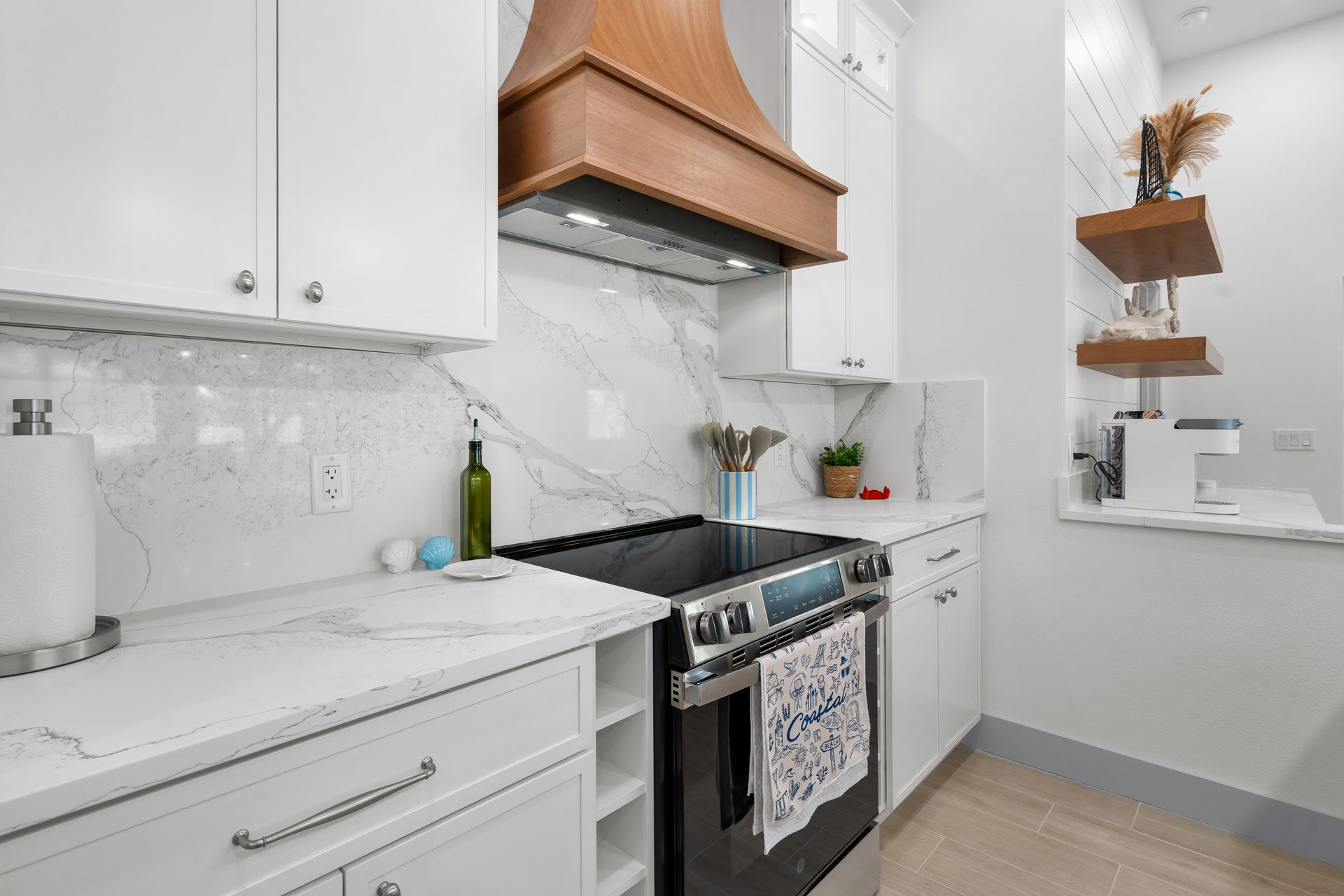 Bright white modern kitchen with marble counters, stainless stove, and copper range hood
