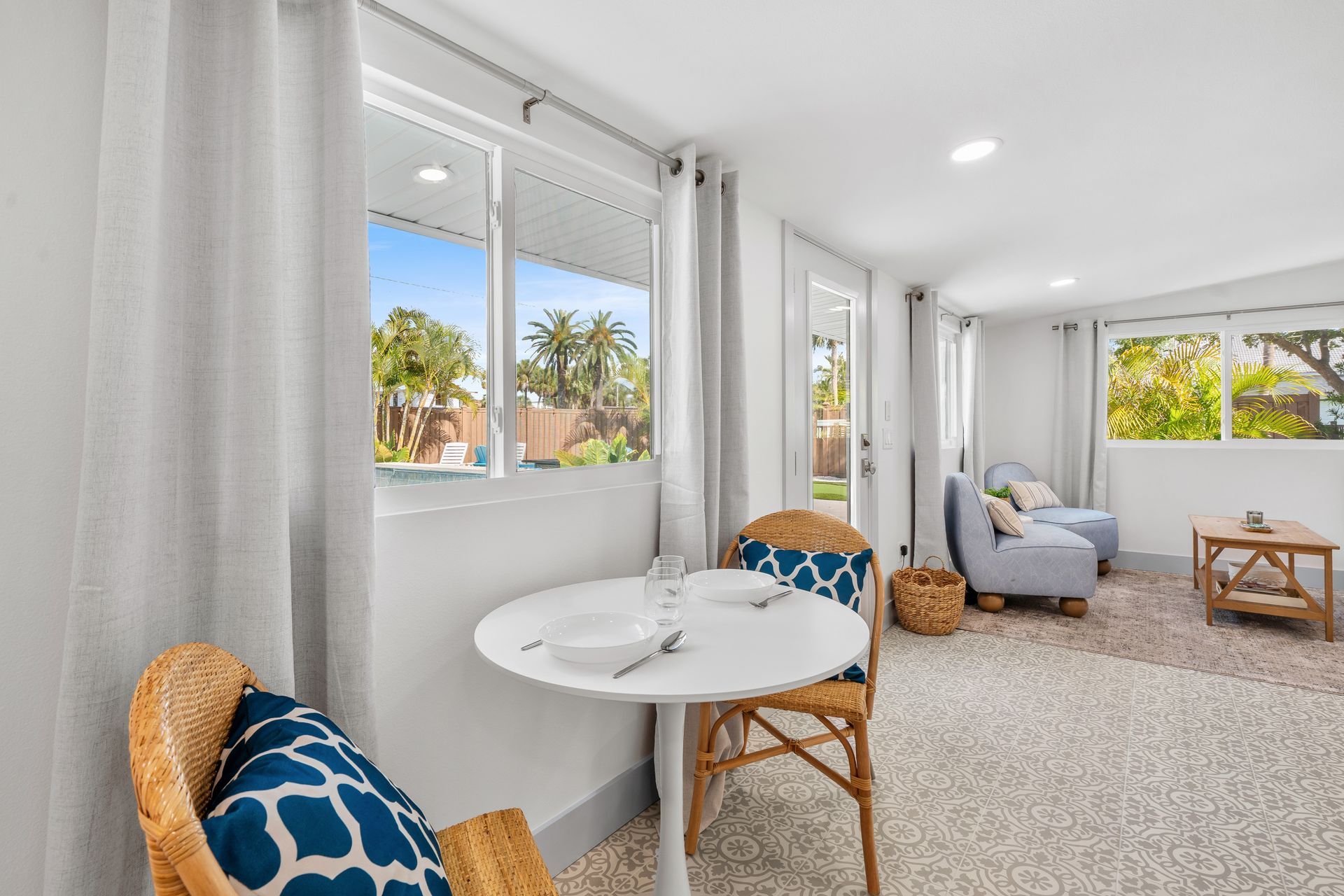 Bright sunroom with white walls, carpet, wicker chairs, and blue cushions by large windows