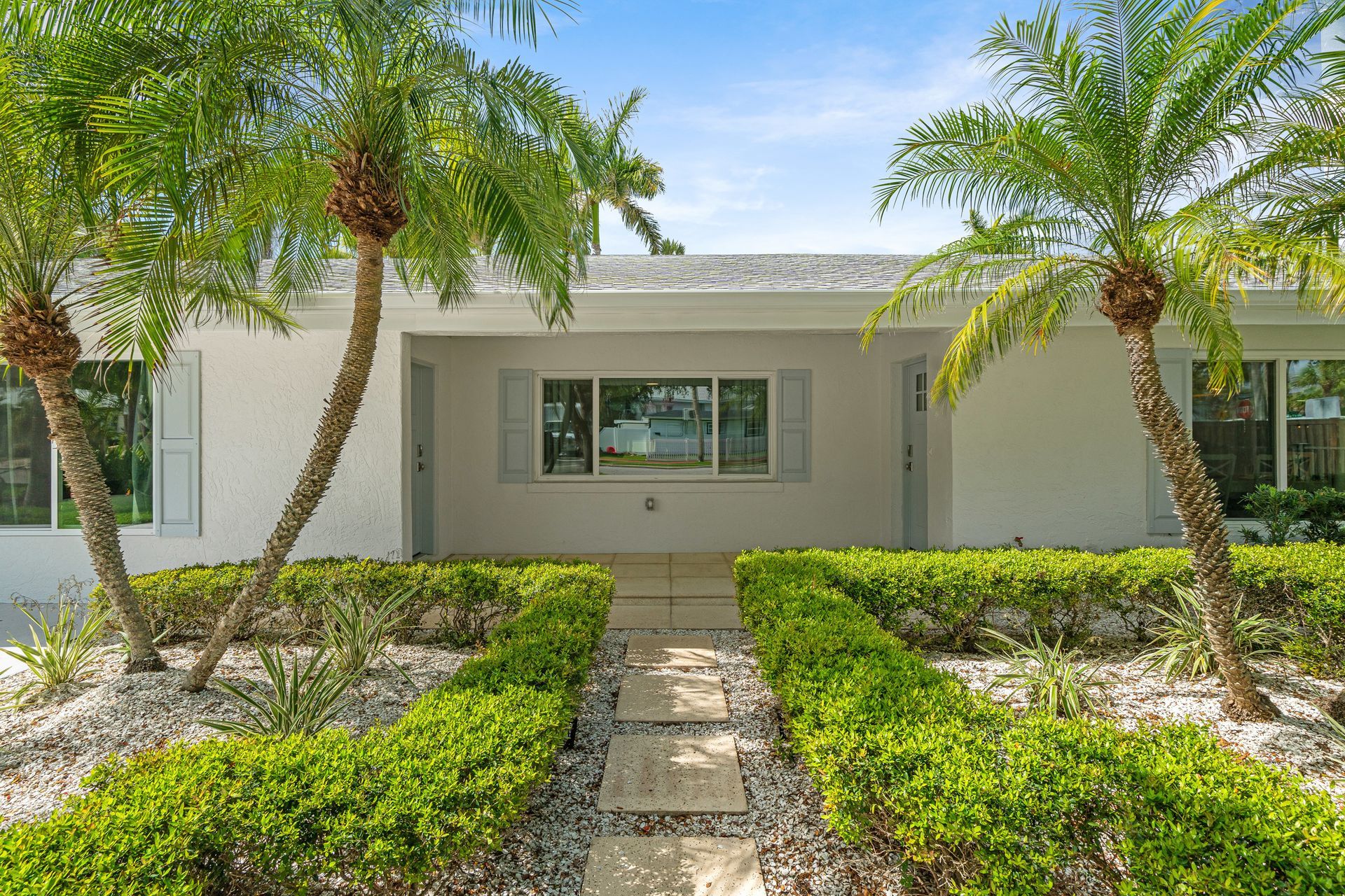 Single-story white house with palm trees and a neatly landscaped front yard