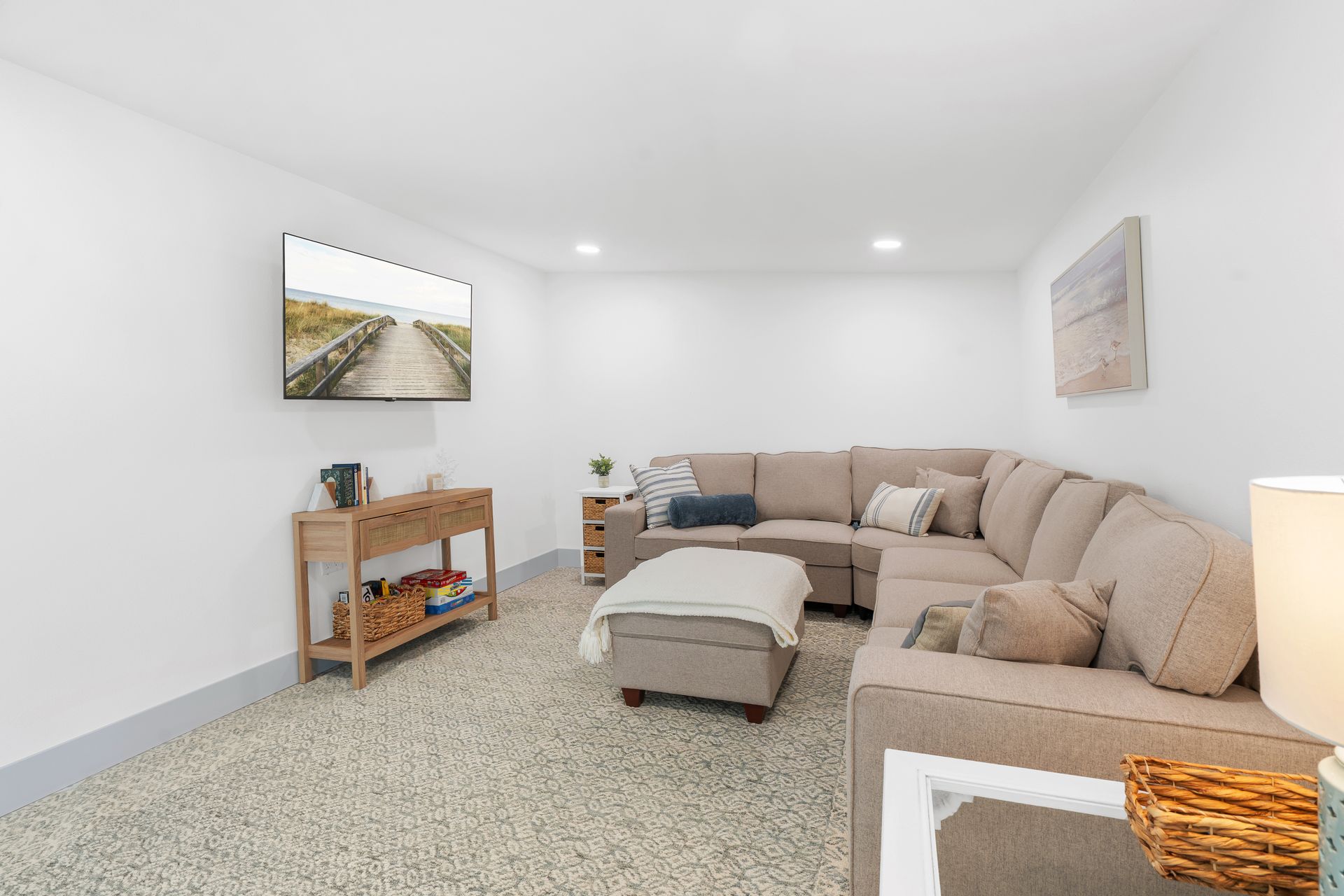 Bright, minimalist living room with beige sectional sofa, ottoman, and wall art in a white-walled space