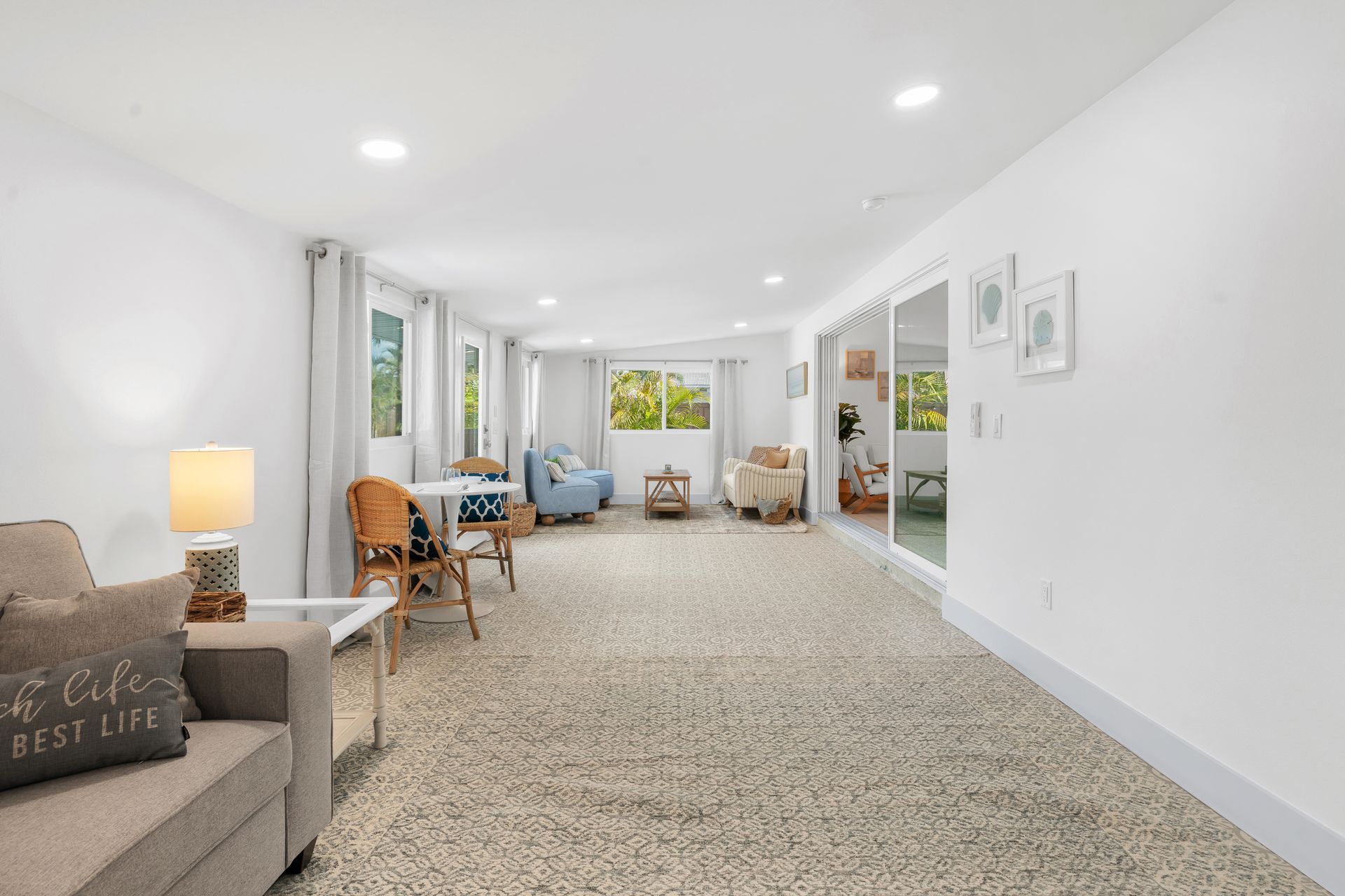 Bright living room with white walls, beige carpet, and chairs by large windows and glass doors.