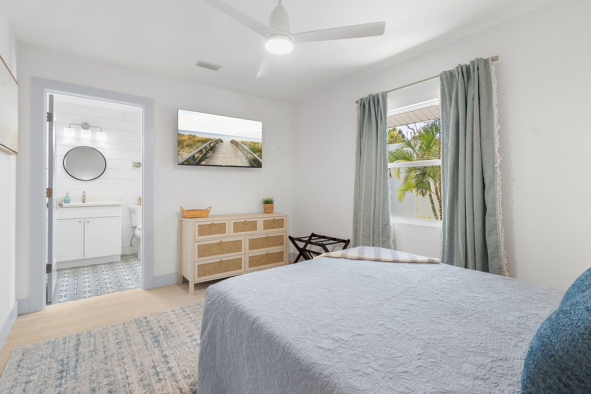 Bright bedroom with white walls, bed, dresser, ceiling fan, and a window with curtains.