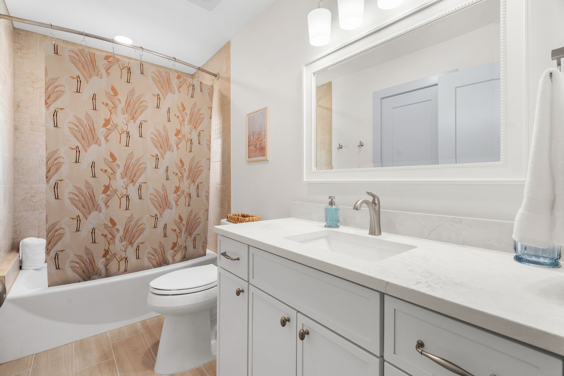 Bright bathroom with floral shower curtain, white vanity, mirror, and bathtub.